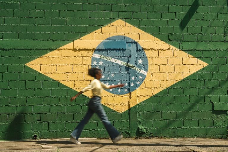 girl walking on street with brazilian flag on wall